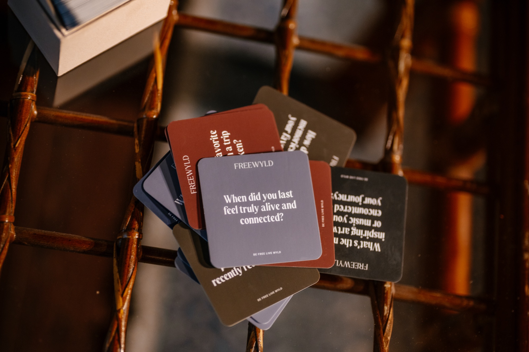Freewyld branded conversation cards fanned across a woven chair, reading 'When did you last feel truly alive and connected?'